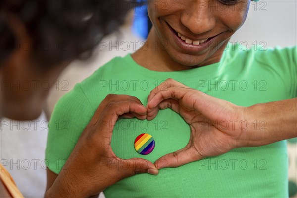 Gay man gesturing heart shape around LGBT badge next to his partner at home