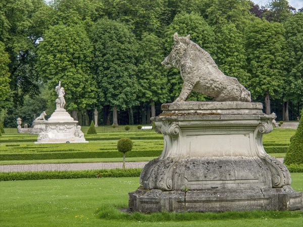 Stone sculpture of a boar in a spacious park with hedges and trees, historic castle with a green
