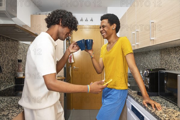 Happy gay couple enjoying coffee and looking at the mobile at home in the morning