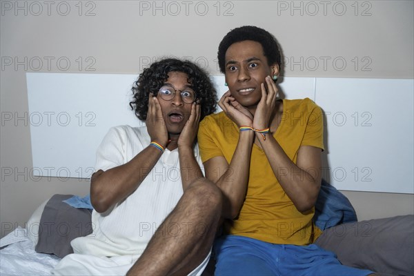 Gay latin male couple watching a horror movie at night at home