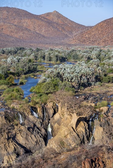 Kunene River with green vegetation in dry red mountain landscape, waterfall and African Baobab