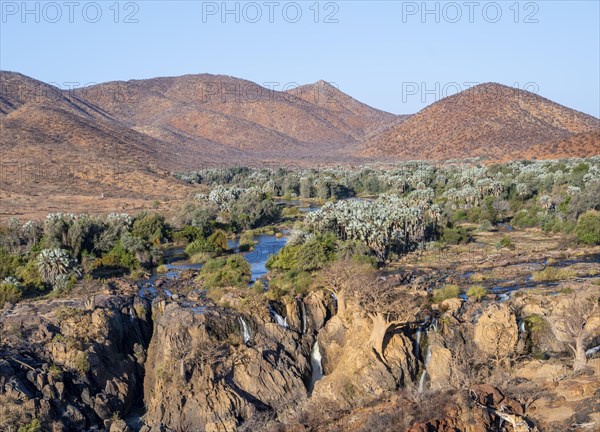 Kunene River with green vegetation in dry red mountain landscape, waterfall and African Baobab
