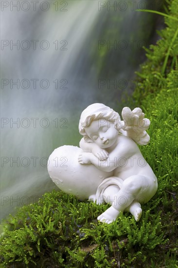 Porcelain angel figurine on moss by a waterfall