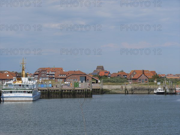 View of a harbour with several ships and houses behind them under a slightly cloudy sky, Baltrum