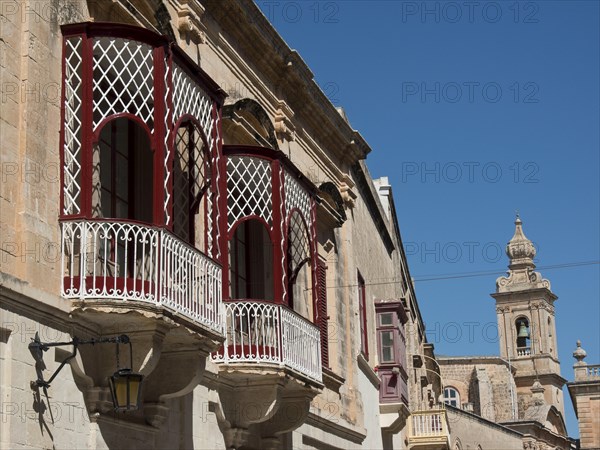 A view of an old town street with several balconies and a church tower in the background,