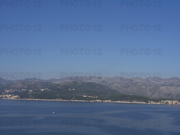 Tranquil coastal landscape with gentle mountains and clear blue skies reflected in the calm sea,