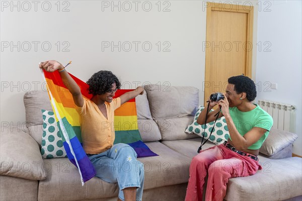 Gay man posing for his couple taking photos raising LGBT rainbow flag at home
