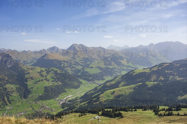 Spacious sunny valley with green meadows and mountains in the background under a blue sky, mountain