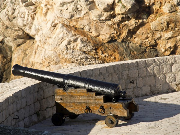 Black cannon on a wooden frame in front of a historic stone wall, the old town of Dubrovnik with