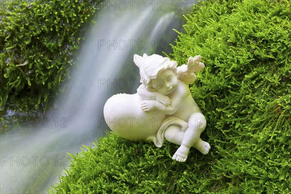 Porcelain angel figurine on moss by a waterfall