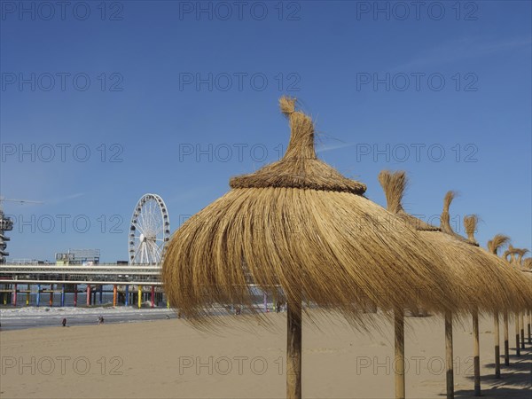 Beach with thatched parasols and a Ferris wheel in the background, parasols and a pier on the beach