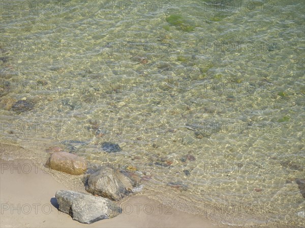 Clear water on the coastal shore with various stones on the sandy beach, spring on the Baltic Sea