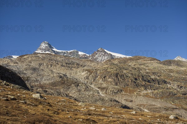 Striking peaks above rocky landscape and sparse snow under clear blue sky, bare mountain peaks with