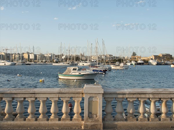 Harbour view with numerous boats on the calm sea and a stone balustrade in the foreground, Valetta,