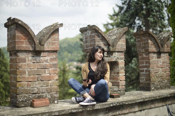 Young woman in casual clothing focused on conversation with smartphone in a peaceful garden with