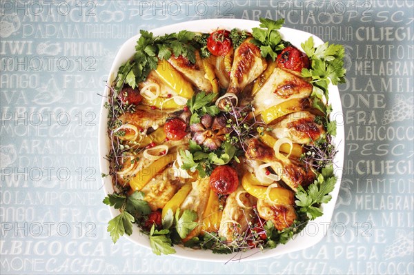 Roasted chicken and bell peppers arranged in a white dish with cherry tomatoes and parsley on a