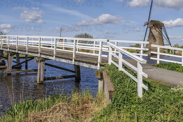 White bridge over a canal, windmill in the background, calm nature-related atmosphere, windmills of