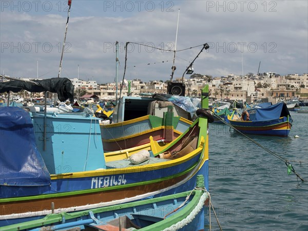 Several fishing boats in the harbour of a town, traditionally painted under a blue sky, many