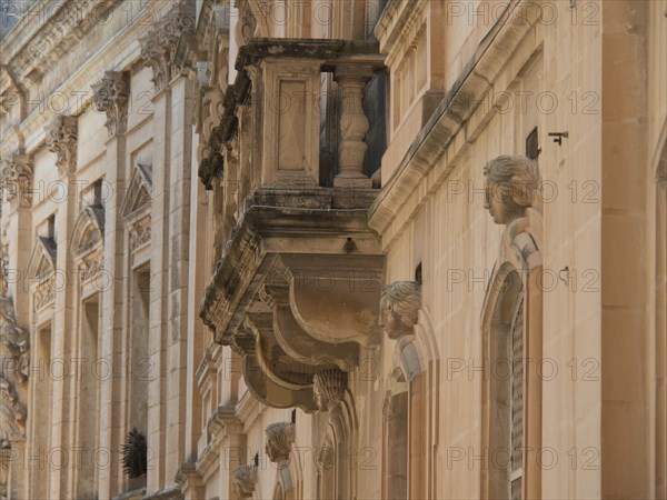Side view of a historic building with decorative sculptures and balconies, the town of mdina on the