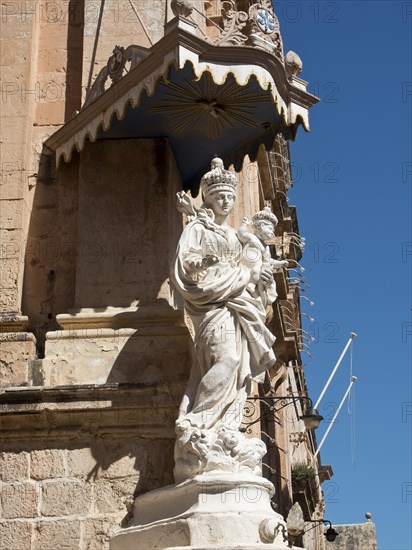 A stone statue of the holy mother and child in front of a historic stone facade, the town of mdina