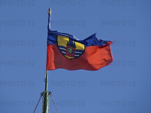 A flag with a coat of arms fluttering vividly in the wind against a clear blue sky, Borkum,