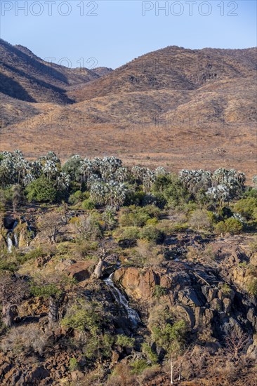 Kunene River with green vegetation in dry red mountain landscape, waterfall and African Baobab