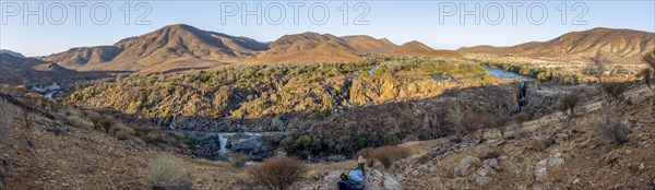 Panorama, Kunene River with green vegetation in dry red mountain landscape, waterfall and African