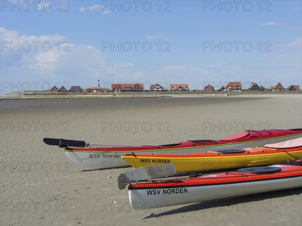 Several kayaks on the beach with a view of a coastal landscape and traditional houses, Baltrum