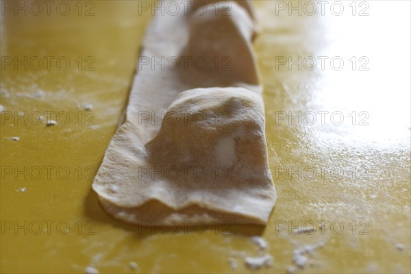Preparation of fresh homemade pasta mezzaluna with ricotta, folded dough in front of cutting out