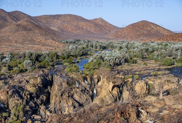 Kunene River with green vegetation in dry red mountain landscape, waterfall and African Baobab