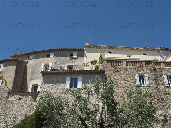 Stone buildings with windows and trees in the foreground under a blue sky, historic stone houses