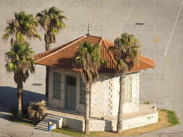 Small pavilion with red roof tiles surrounded by palm trees on an asphalted area, Ancient building