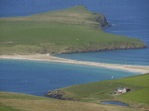 Picturesque coastal landscape with golden sandy beach and lonely house on the green slope in the