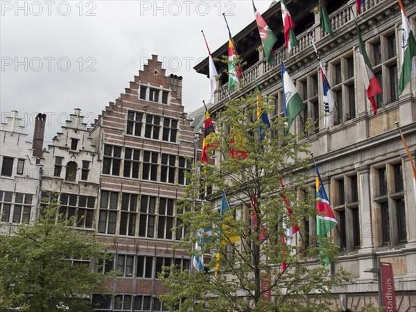Historic buildings with ornate gables and many flags, trees in front under a gloomy sky, Historic