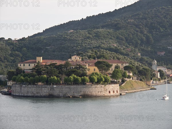 Fortress on the water with a sailing boat in the foreground, surrounded by trees and hills, Bari,