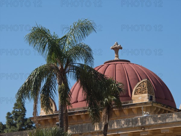 Historic building with red dome behind palm trees in front of a bright blue sky, palermo in sicily