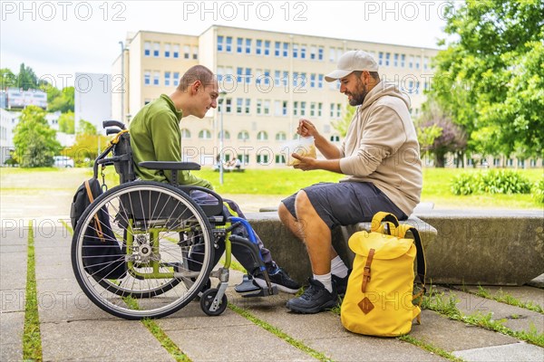 Man helping to eat to a man with cerebral palsy in a wheelchair in the university campus