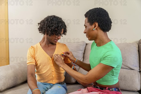 A gay man pinning an LGBT flag badge onto his partner's shirt at home