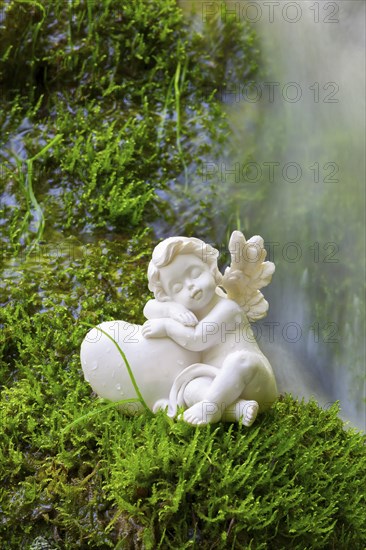 Porcelain angel figurine on moss by a waterfall