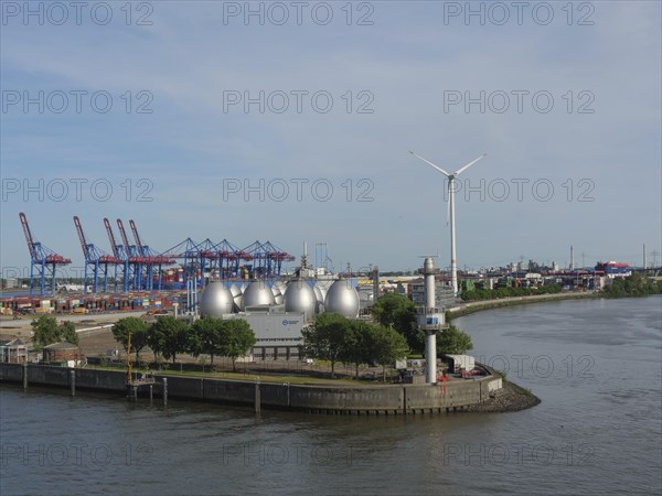 Harbour view with wind power plant, spherical tanks, containers and green trees under a clear sky,