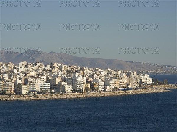 Coastal city skyline with many buildings bordering the blue sea and mountains in the background