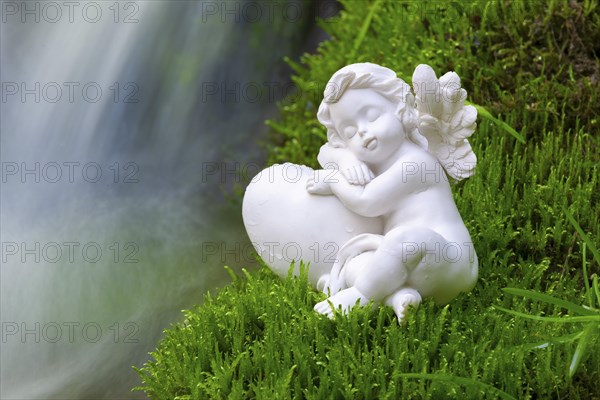 Porcelain angel figurine on moss by a waterfall