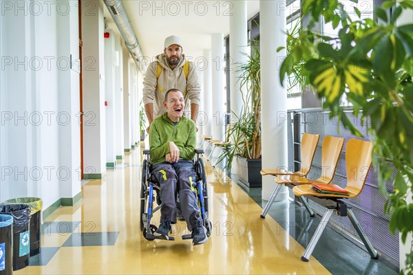 Male friend helping a man with disability in wheelchair to move around the university