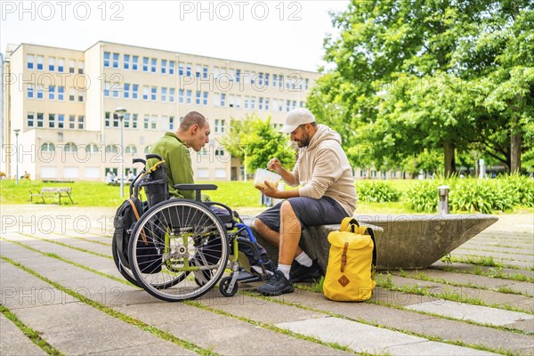 University student helping and eating with a disabled friend in the campus