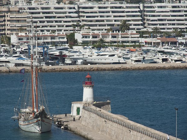 Harbour with a large sailing ship and a lighthouse, surrounded by blue buildings and yachts, ibiza,