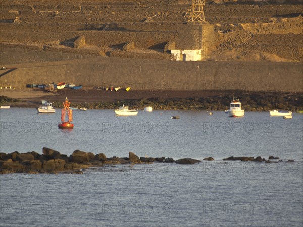 Boats and buoys on the sea in front of a rocky coastline at sunset, Lanzarote with a hisotric