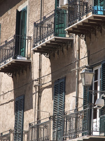 Buildings with green shutters and iron balconies, lanterns on the facade, shadow play on the wall,