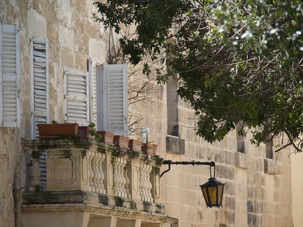 Mediterranean balcony with plants and open shutters, next to it a lantern on an old stone wall,