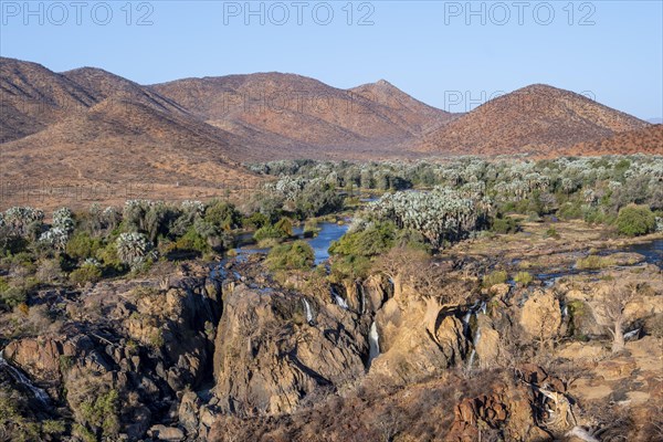 Kunene River with green vegetation in dry red mountain landscape, waterfall and African Baobab
