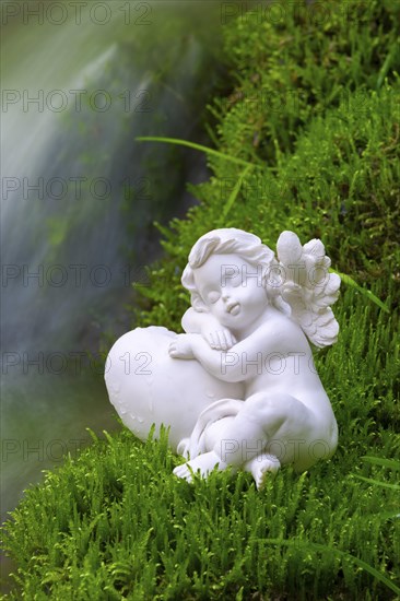 Porcelain angel figurine on moss by a waterfall